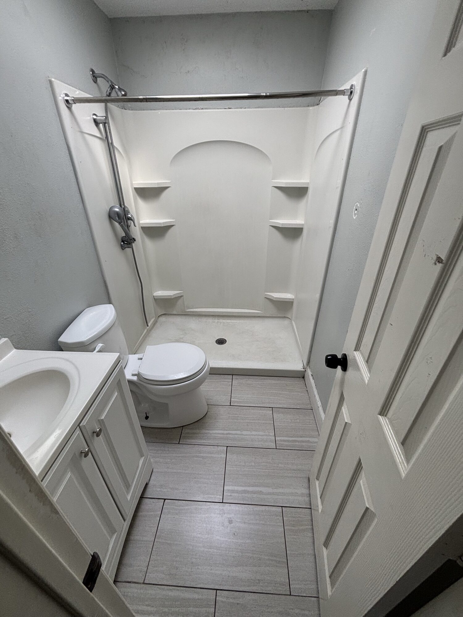 Same bathroom rebuilt clean after OSR demolition and haul-away — new tile floor, shower stall, toilet and vanity in place