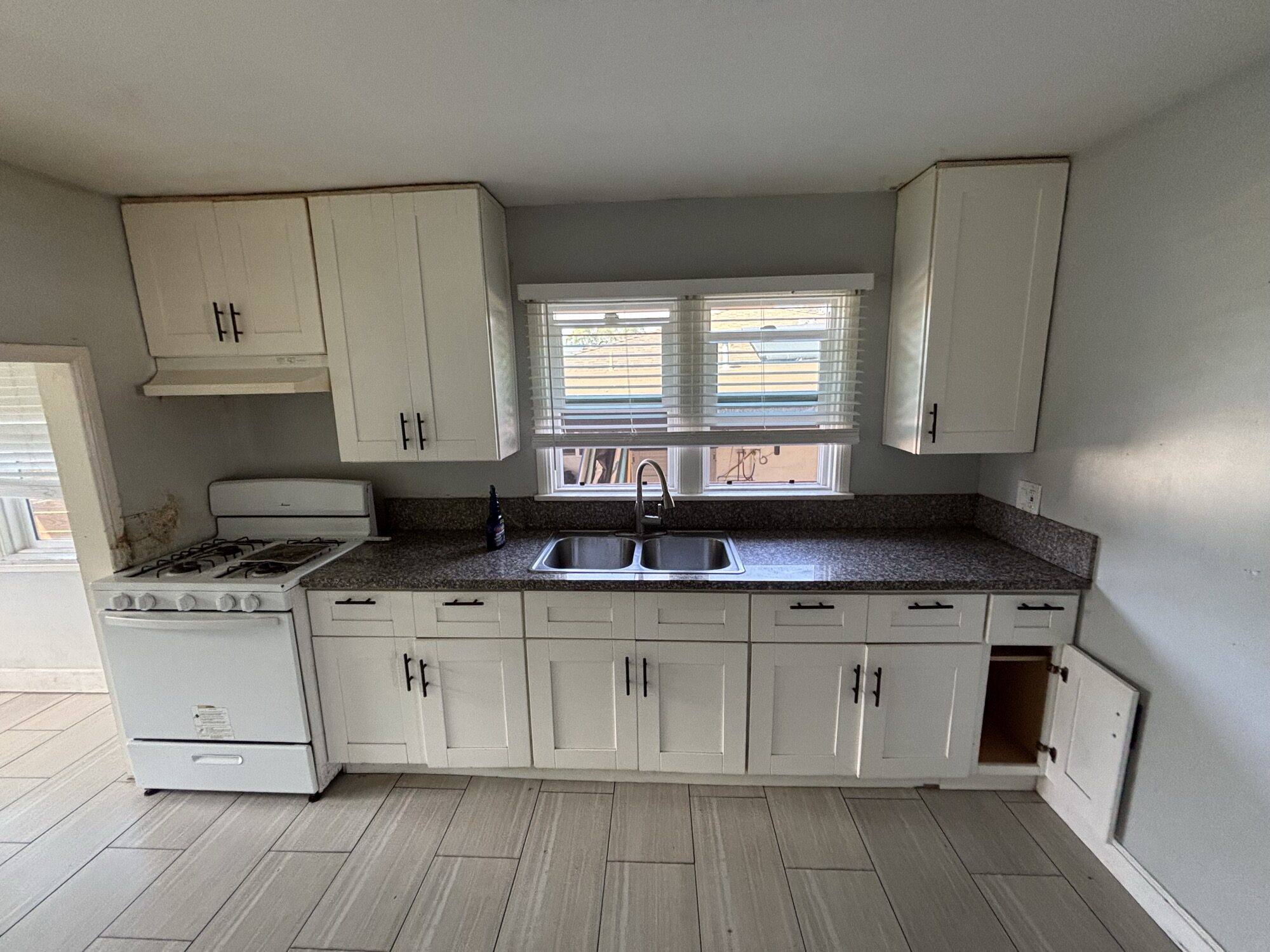 Same kitchen after OSR demolition and haul-away — cleared space with new cabinets, sink, range and tile floor in place